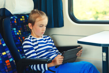 Cute child playing video games online on tablet during trip. Kid travels on a train.
