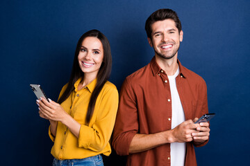 Photo of two funny cheerful people toothy smile use smart phone write blog post isolated on blue...