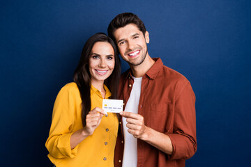 Photo of two cheerful satisfied people toothy smile hands hold demonstrate plastic debit card isolated on blue color background