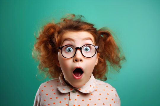 Naklejki Excited, shock, omg wow expression. Shocked surprised funny elementary school kid girl in glasses looking at camera, sitting on bright green background. Promo offer banner, adverts concept