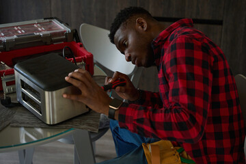 Curly-haired repairman is repairing a toaster on the kitchen table