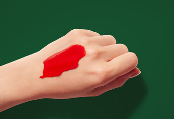 Red cosmetic texture smudge on woman hand dark purple background