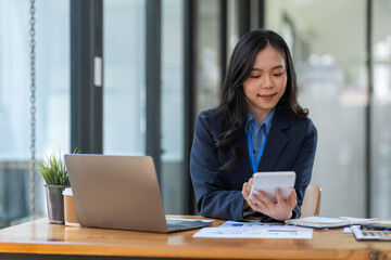 Asian businesswoman smiling at the idea of ​​working at a calculator to calculate income. on the laptop at the office.