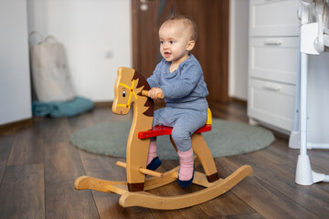 Happy baby girl playing on wooden rocking horse. Childhood, game at home concept