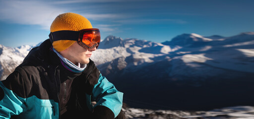 young man in ski goggles on a snowy mountain on a sunny day. close-up of a man looking to the side,...