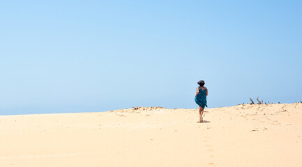 Fototapeta na wymiar Latino Woman Running Across A Sand Hill Toward Blue Sky.JPG