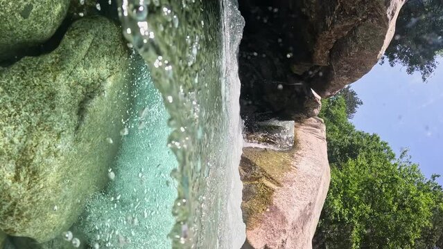 VERTICAL VIDEO, Water flows between the stones forming small waterfalls and baths. Stream with crystal clear water and bubbles. Half underwater slow motion shot