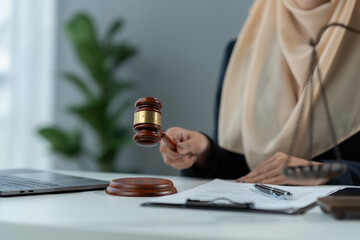 female Muslim lawyer wearing hijab holding the hammer of justice Summary of business contract legal terms in a valid document with investment signing on desk inside the office.