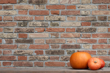 Background of a wall made of red fired bricks with three orange pumpkins lying on the side. There...