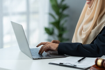 female lawyer Muslim wearing hijab working on business contract documents with laptop and reading law book Take notes to check the accuracy of justice. Legal services concept in the office.