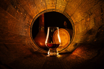 A glass of scotch whiskey in old oak barrel. Copper alambic and small barrel on background....