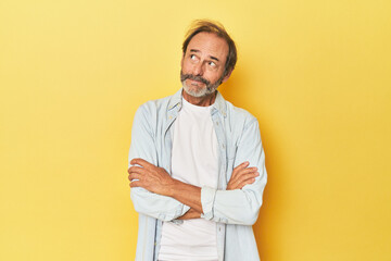 Caucasian middle-aged man in yellow studio dreaming of achieving goals and purposes