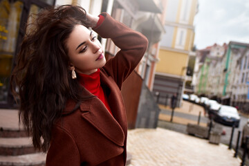 Charming woman in a brown coat on the street straightens her hair.