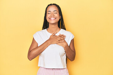Young Indonesian woman on yellow studio backdrop laughing keeping hands on heart, concept of...