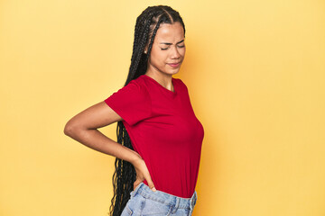 Young Indonesian woman on yellow studio backdrop suffering a back pain.