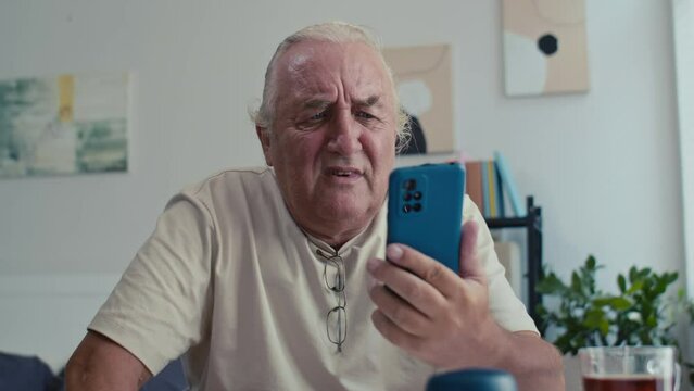 Medium shot of sad senior man having problems when using modern smartphone at home