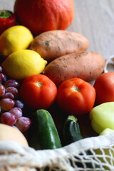 Reusable mesh bag with seasonal fruit and vegetable on wooden background. Late summer or early autumn. Selective focus.