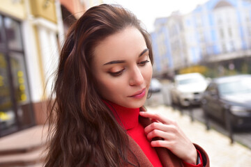 Portrait of a beautiful dreaming lady in a brown autumn coat on the street.