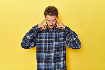 Young Caucasian man on a yellow studio background focused on a task, keeping forefingers pointing head.