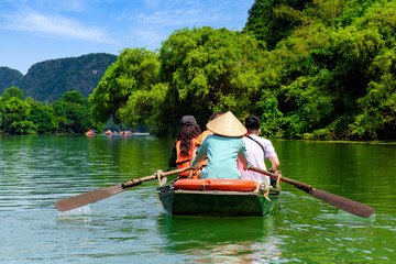 Tourists sitting on rowing boats enjoy the beautiful scenery of rivers and mountains in Trang An, Ninh Binh province, Vietnam.	