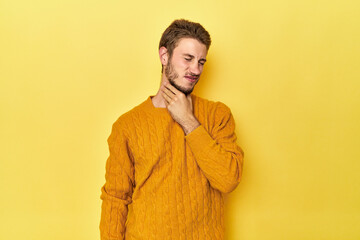 Young Caucasian man on a yellow studio background suffers pain in throat due a virus or infection.