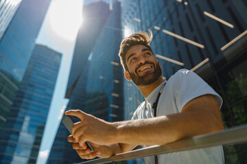 Handsome man standing on skyscrapers background and listen music in headphones and looks away