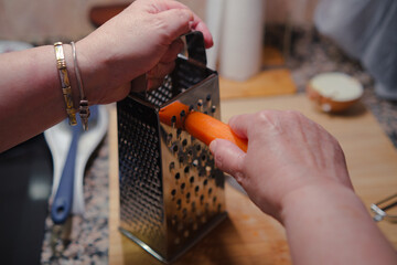 Closeup of hands grating fresh carrots. Cooking healthy food.