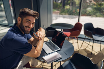 Handsome smiling entrepreneur working on laptop sitting in coworking during working day