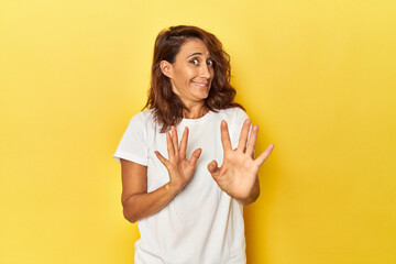 Middle-aged woman on a yellow backdrop rejecting someone showing a gesture of disgust.