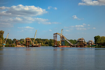 Panoramic landscape view the process of mounting steel structures for construction of a new pedestrian bridge over river. Bridge under construction. Obolon neighborhood in Kyiv, Ukraine