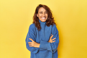 Middle-aged woman on a yellow backdrop laughing and having fun.