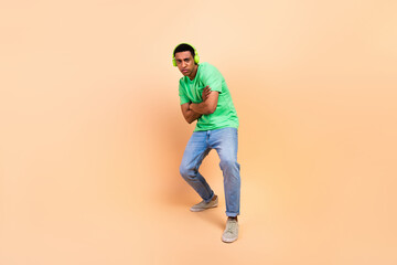 Fototapeta na wymiar Full size photo of stylish guy dressed green t-shirt denim pants posing in headphones arms crossed isolated on beige color background