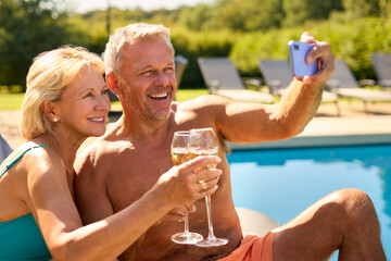 Senior Couple On Holiday Posing For Selfie Drinking Champagne Relaxing By Hotel Swimming Pool