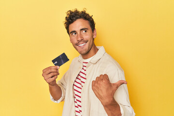 Man holding credit card on yellow points with thumb finger away, laughing and carefree.