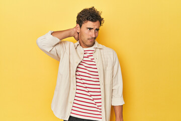 Young Latino man posing on yellow background touching back of head, thinking and making a choice.