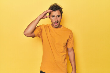 Fototapeta na wymiar Young Latino man posing on yellow background shouts loud, keeps eyes opened and hands tense.