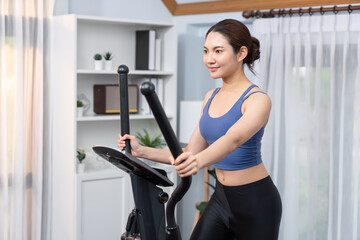 Energetic and strong athletic asian woman running on elliptical running machine at home. Pursuit of...
