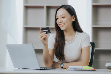 Happy Asian businesswoman paying online using mobile phone and laptop at office