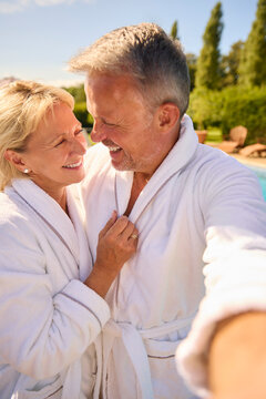 POV Shot Of Senior Couple In Robes Outdoors By Swimming Pool On Spa Day