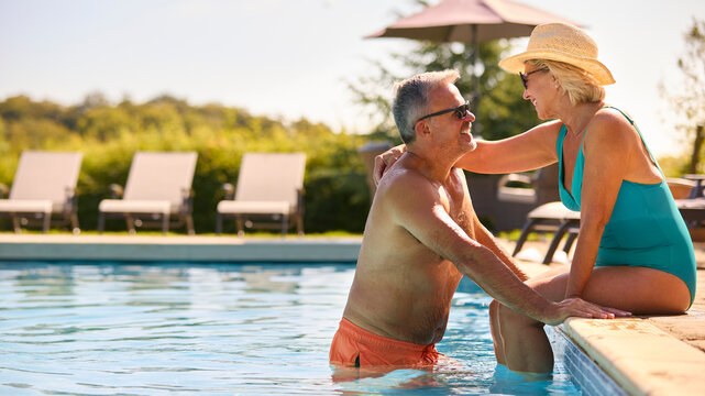 Loving Senior Couple On Holiday Wearing Swimming Costumes Relaxing By Hotel Swimming Pool