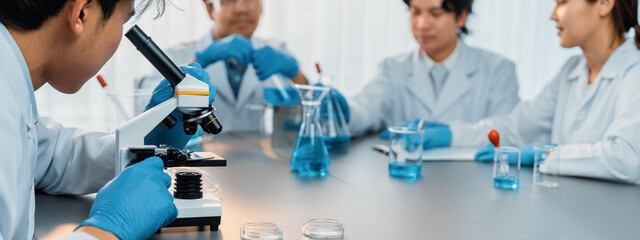 Group of dedicated scientist conduct chemical experiment using microscope in medical laboratory to...