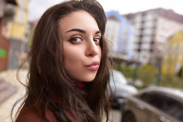 Obraz premium A beautiful fashionable woman in an autumn brown coat sends a kiss on the street.