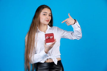 Pretty fair hair lady in shirt pointing at lovely gift box, while looking at camera. Portrait of...