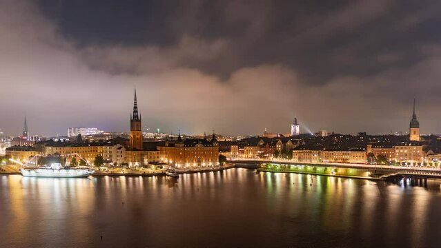 Time lapse Stockholm Sweden: city lights, night view of Stadsholmen district (Gamla Stan) and Riddarholmen district, buildings reflected in the water. Cityscape with illumination, Riddarfjarden marina