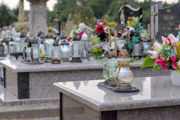 Granitowe nagrobki na starym zabytkowym cmentarzu w Mominie. Groby z kwiatami i płonącymi...