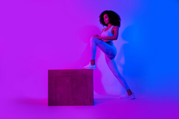Full length cadre of physical activity sport trainer young girl stretch step box platform practicing exercise isolated on neon background