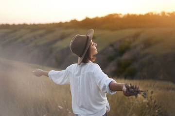 Amazing autumn hillside landscapes with elegance stylish young woman in hat wit open arms enjoying warm sunset in nature