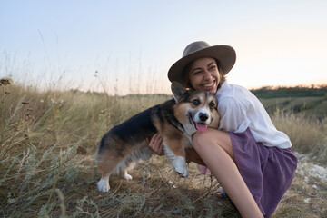 Cute funny Welsh Corgi dog embracing with owner woman amidst a vibrant field