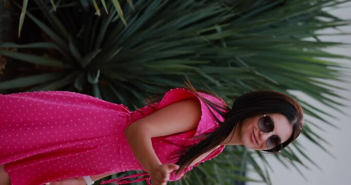 Beautiful woman in pink dress blows a kiss at yucca plant, slow motion vertical video
