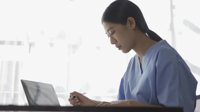 Young Asian nurse working on patient documents at her desk alone in the hospital
